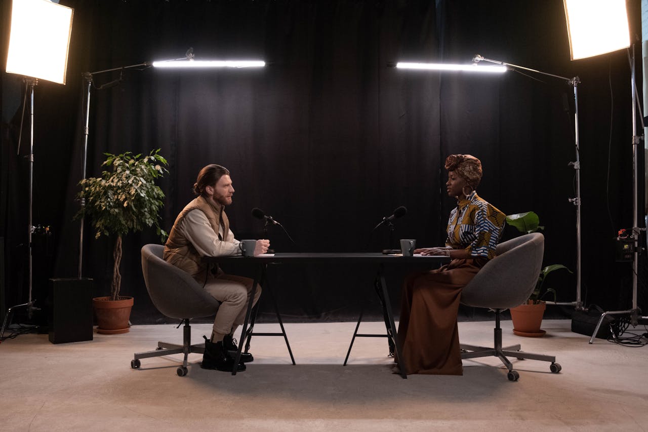 Two hosts recording a podcast in a well-lit studio setup with microphones and studio lights.